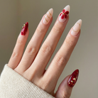 Hand with red and gold nail art on a neutral background