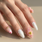 Hand with decorative nails featuring flowers and gold accents on a neutral background