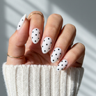 Hand with polka dot nail design wearing a white sweater against a gray background