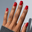 Hand with red nail polish wearing a silver ring on a neutral background