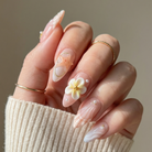 Hand with floral nail art wearing a beige sweater against a neutral background