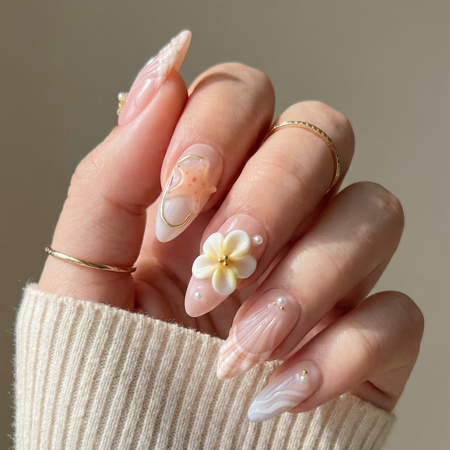 Hand with floral nail art wearing a beige sweater against a neutral background