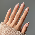 Hand with decorated nails wearing a textured beige sleeve against a gray background